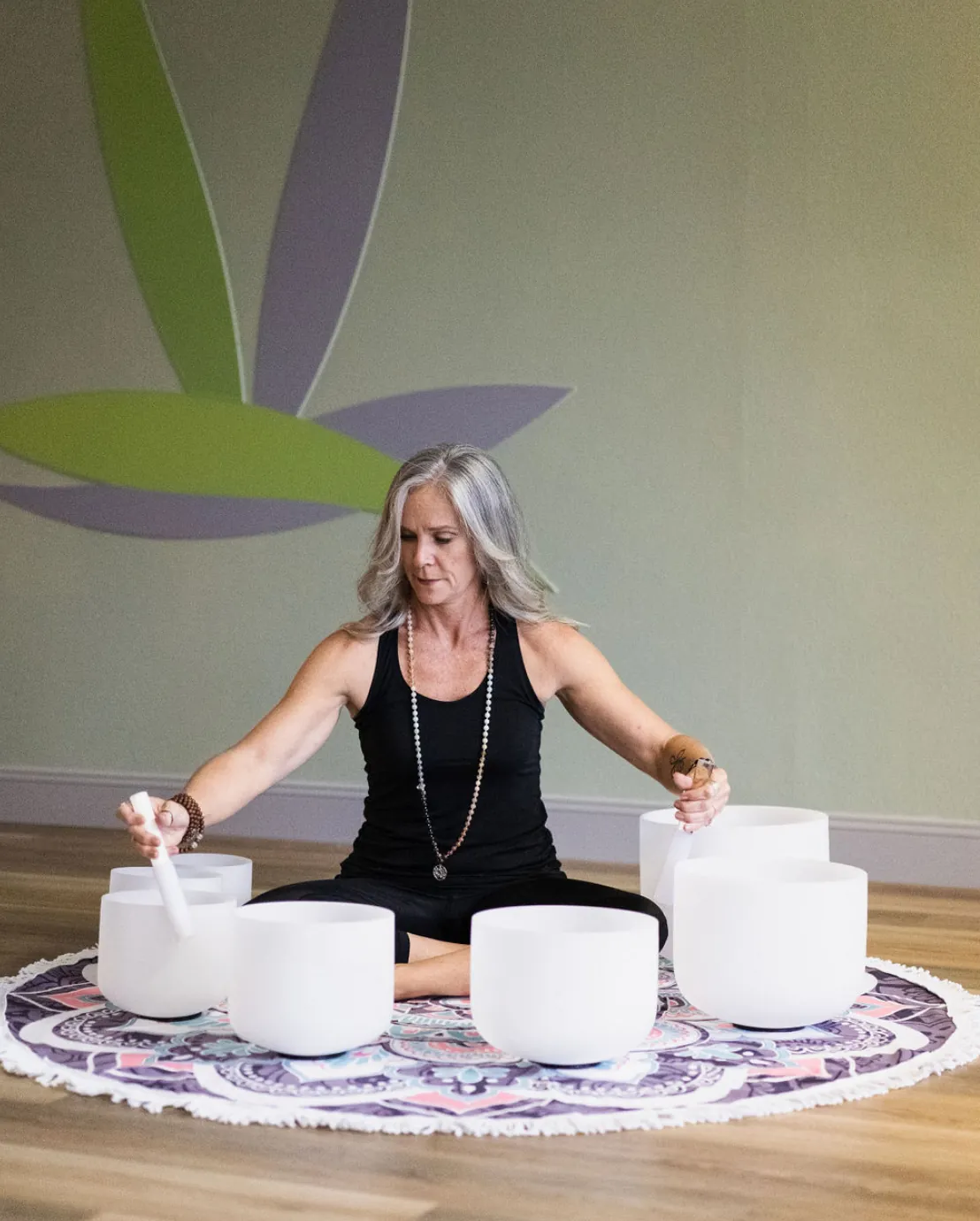 Jill seated among crystal singing bowls in front of the studio logo mural.