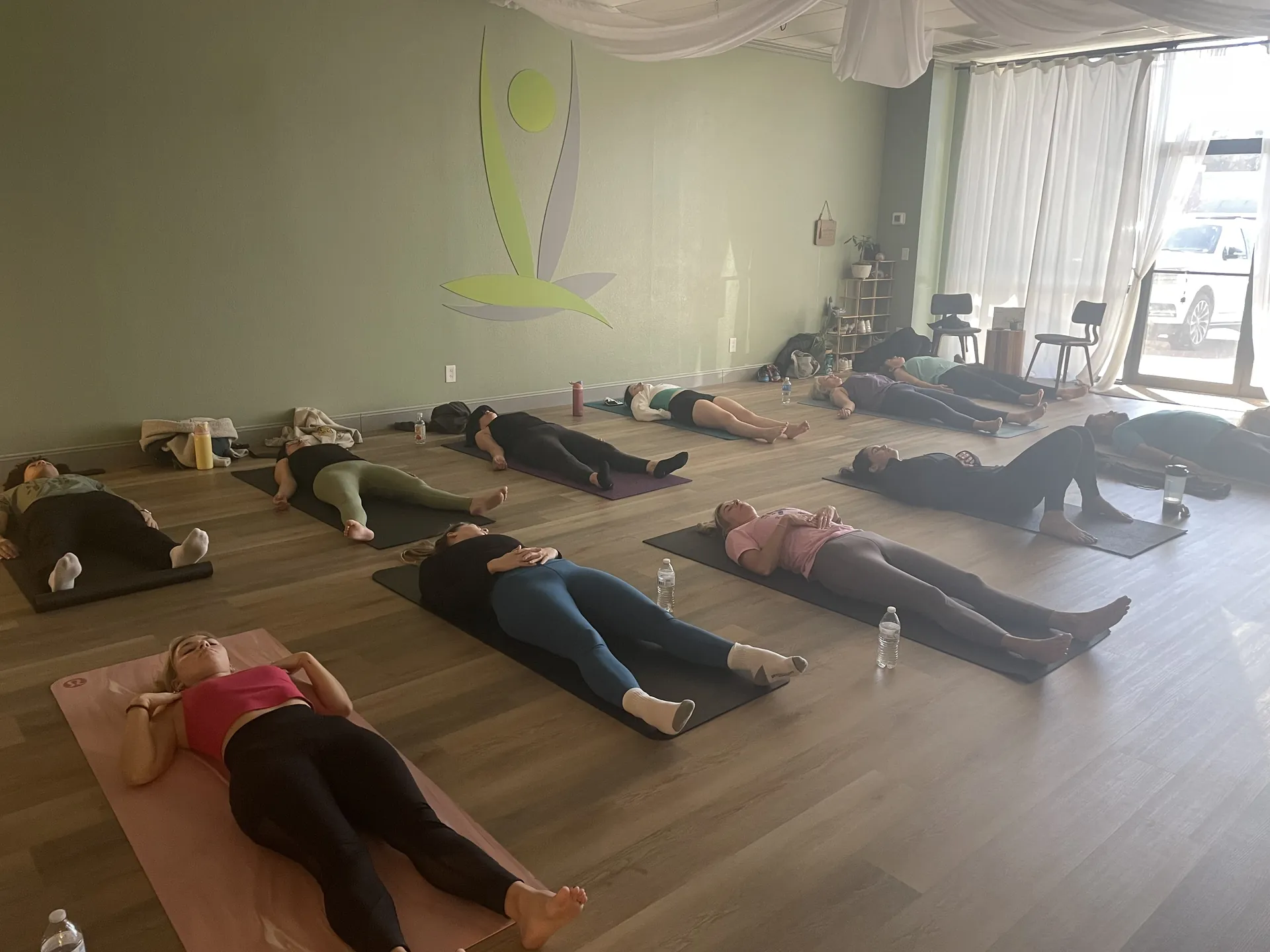 Students resting in savasana at the end of class, beneath the logo mural.