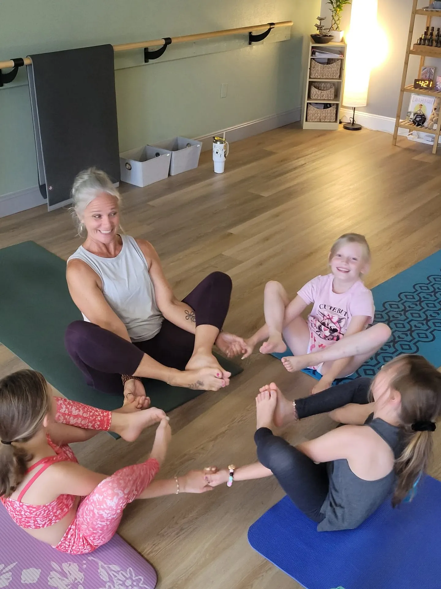 Jill and a circle of children in boat pose together during a kids yoga class.