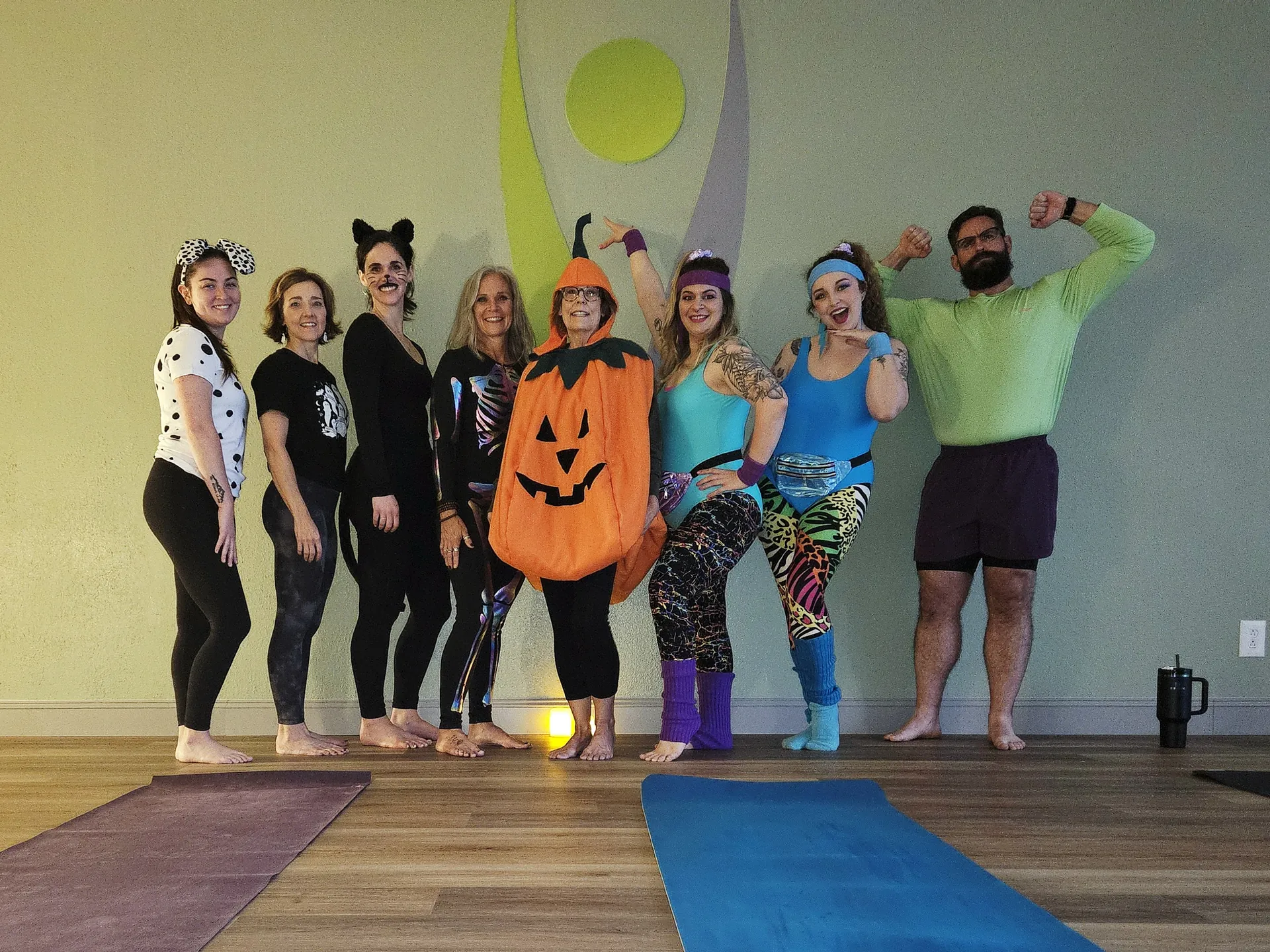 The class in costume for the Halloween Stretch & Treat practice, lined up in front of the logo mural.