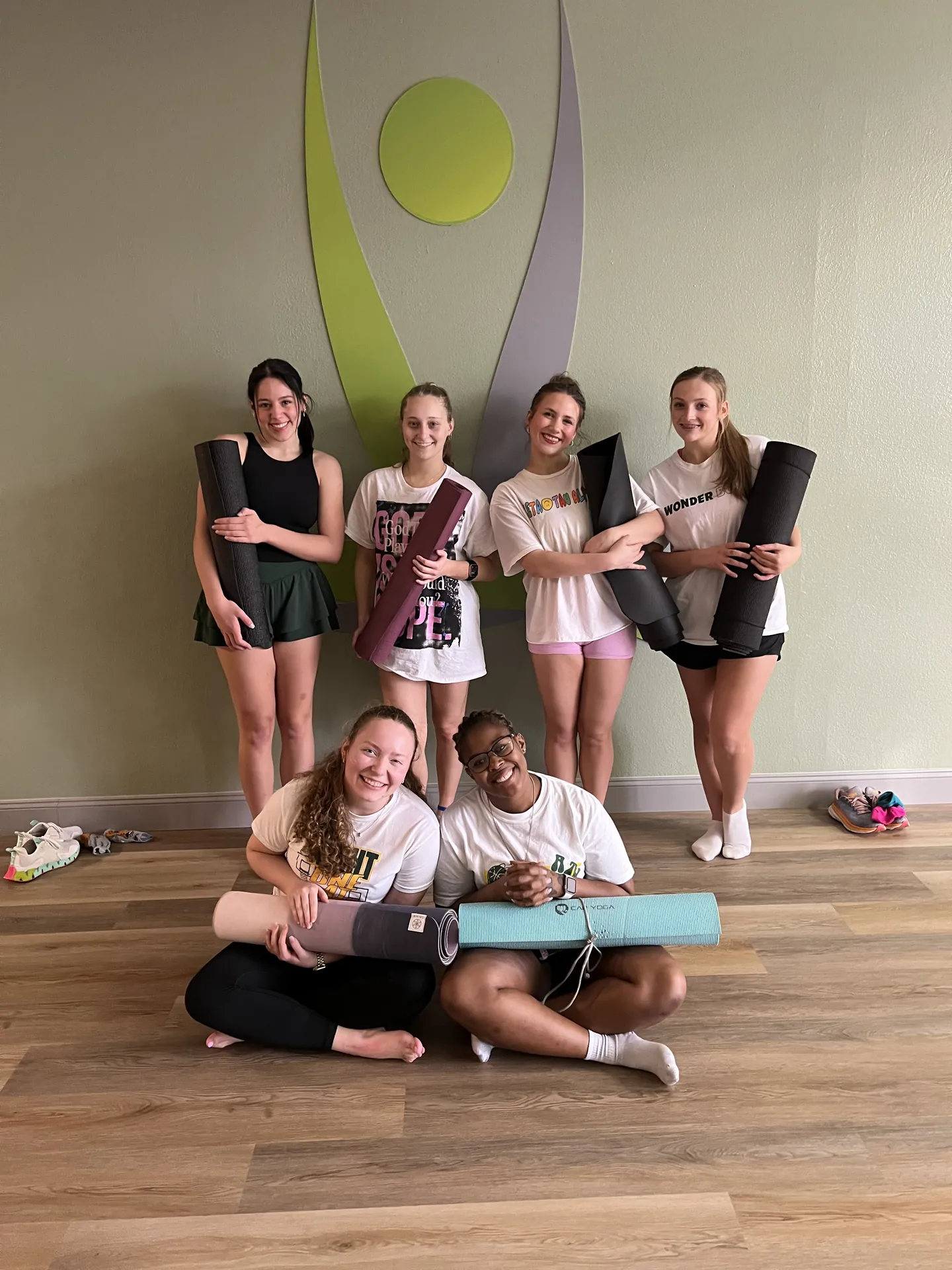 A group of students holding their mats in front of the logo mural.