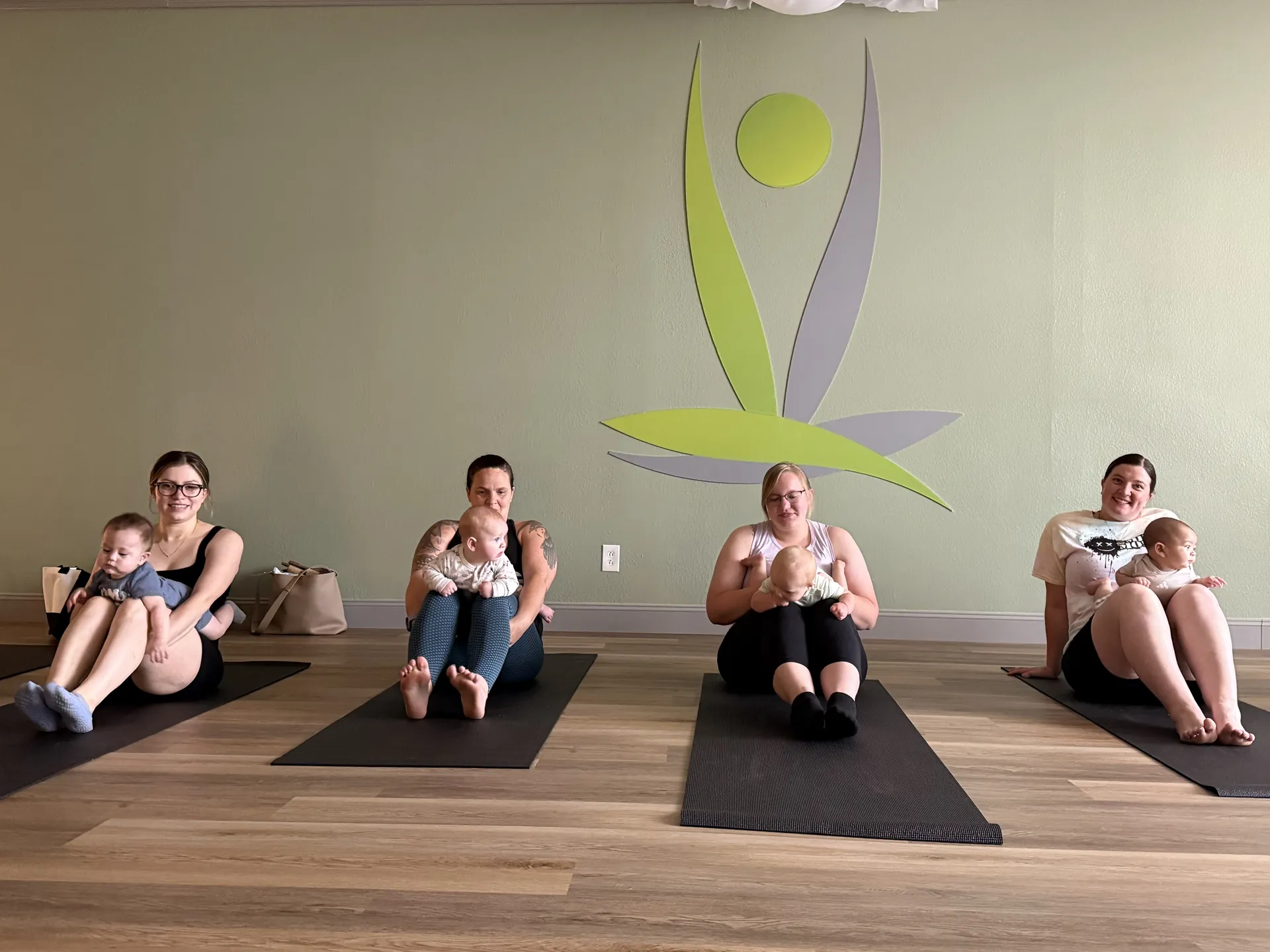 Mom and Mini yoga: mothers seated with their babies in front of the mural.