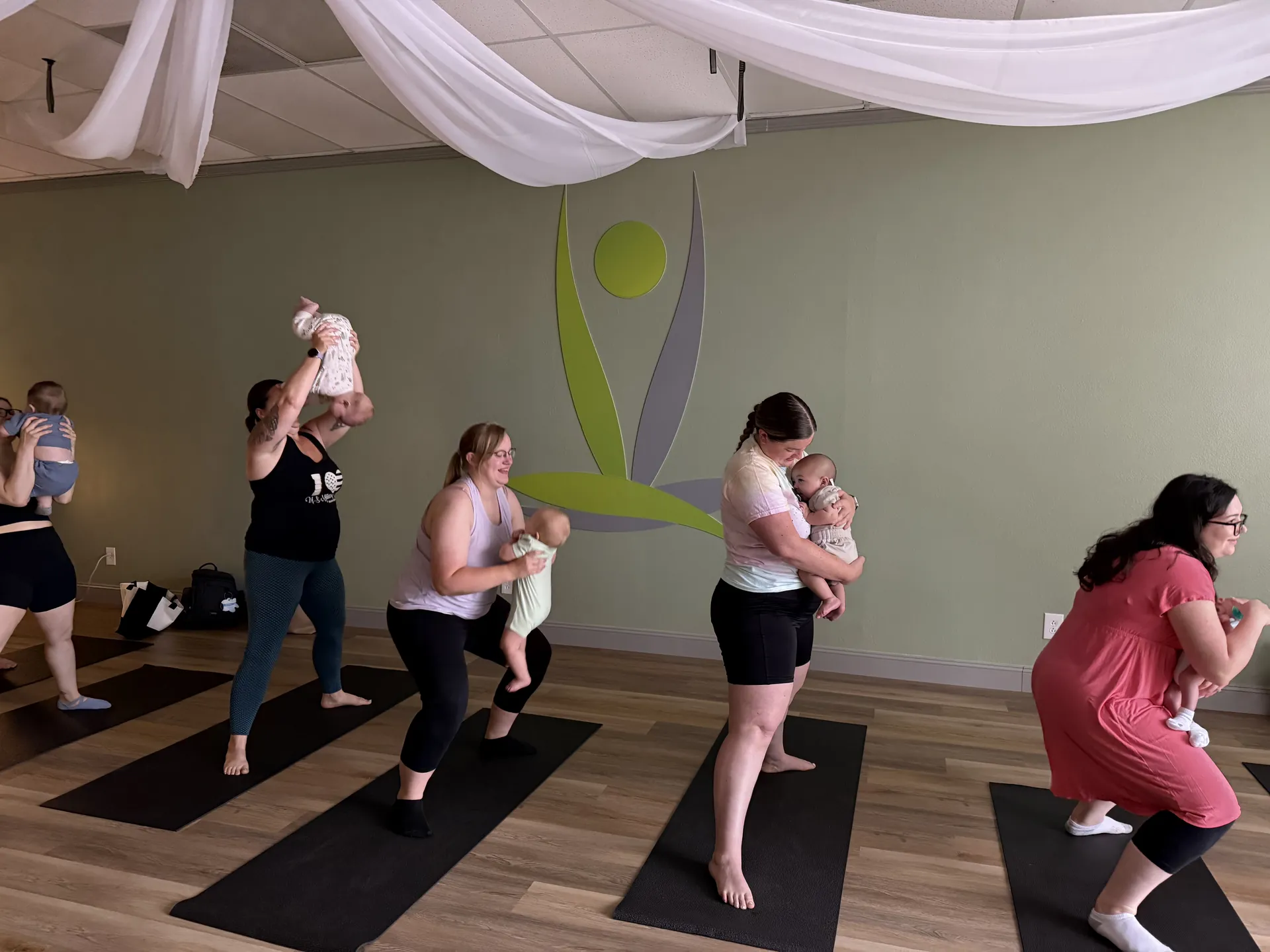 Mothers holding their babies in a standing pose during Mom and Mini yoga.