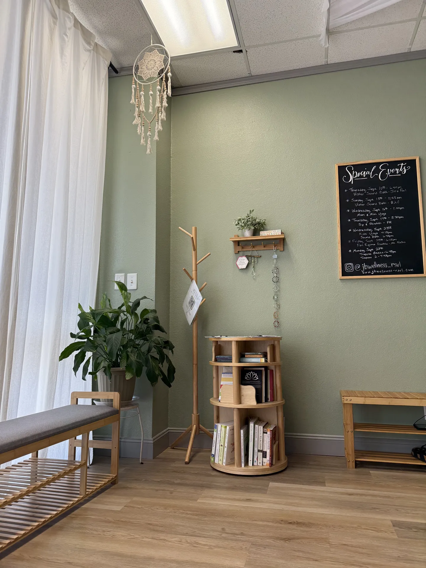 The studio entrance corner: the lending library, a bench, a plant and the events chalkboard by the window.