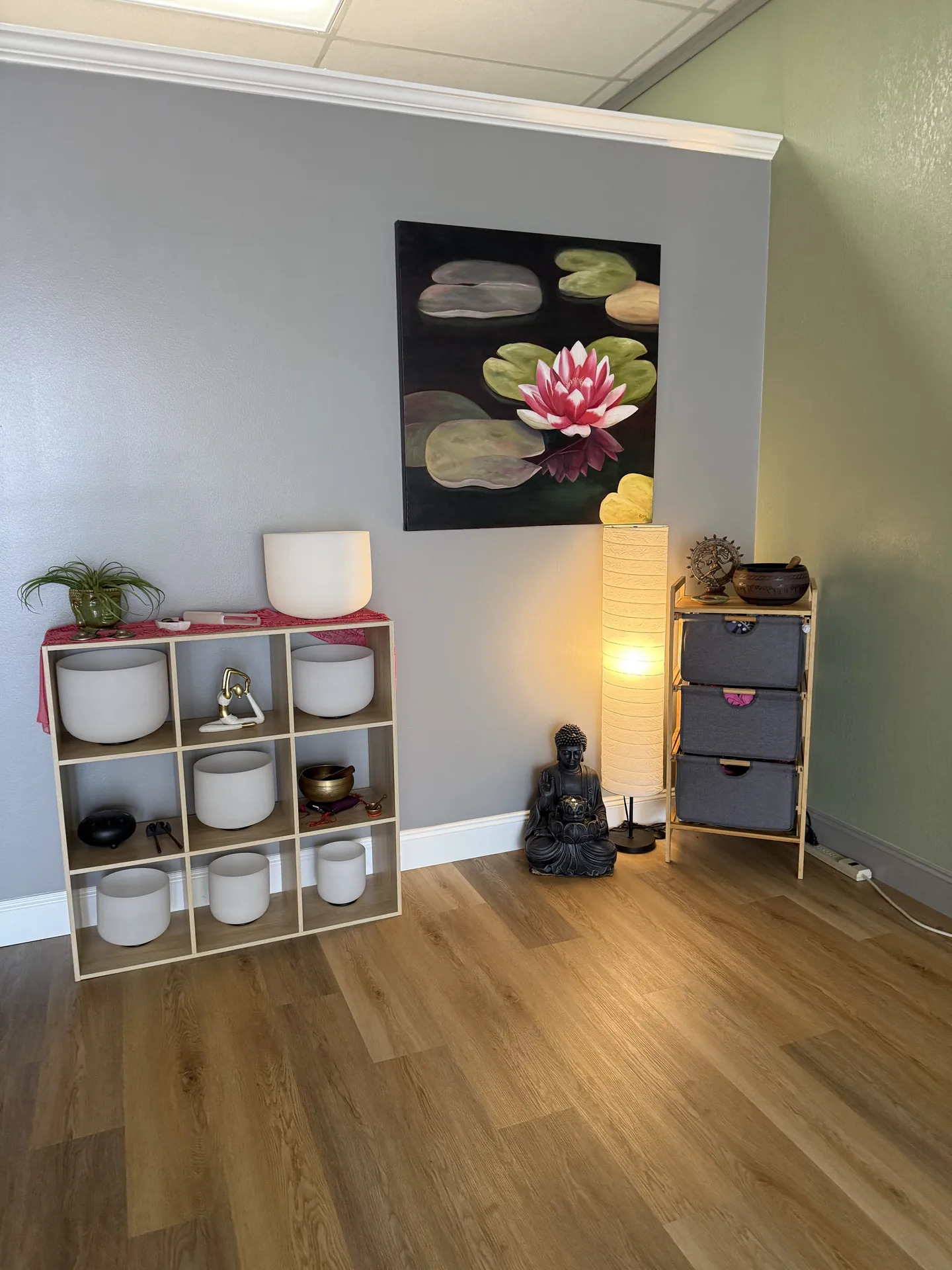 The singing-bowl shelf with a lamp and a small Buddha figure beneath a lotus painting.