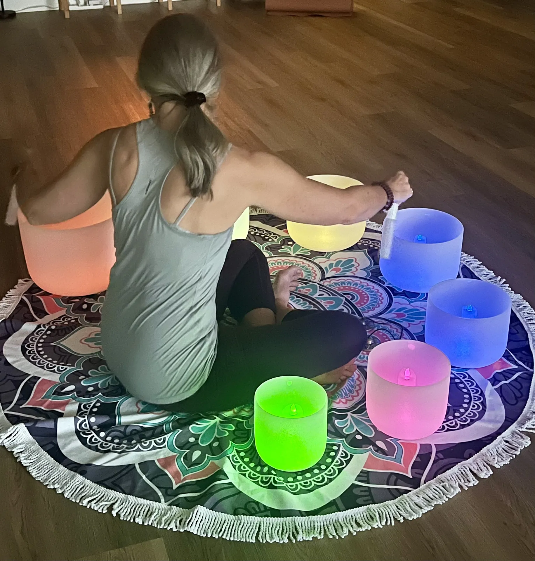 Jill playing illuminated crystal singing bowls on a mandala rug during a sound bath.