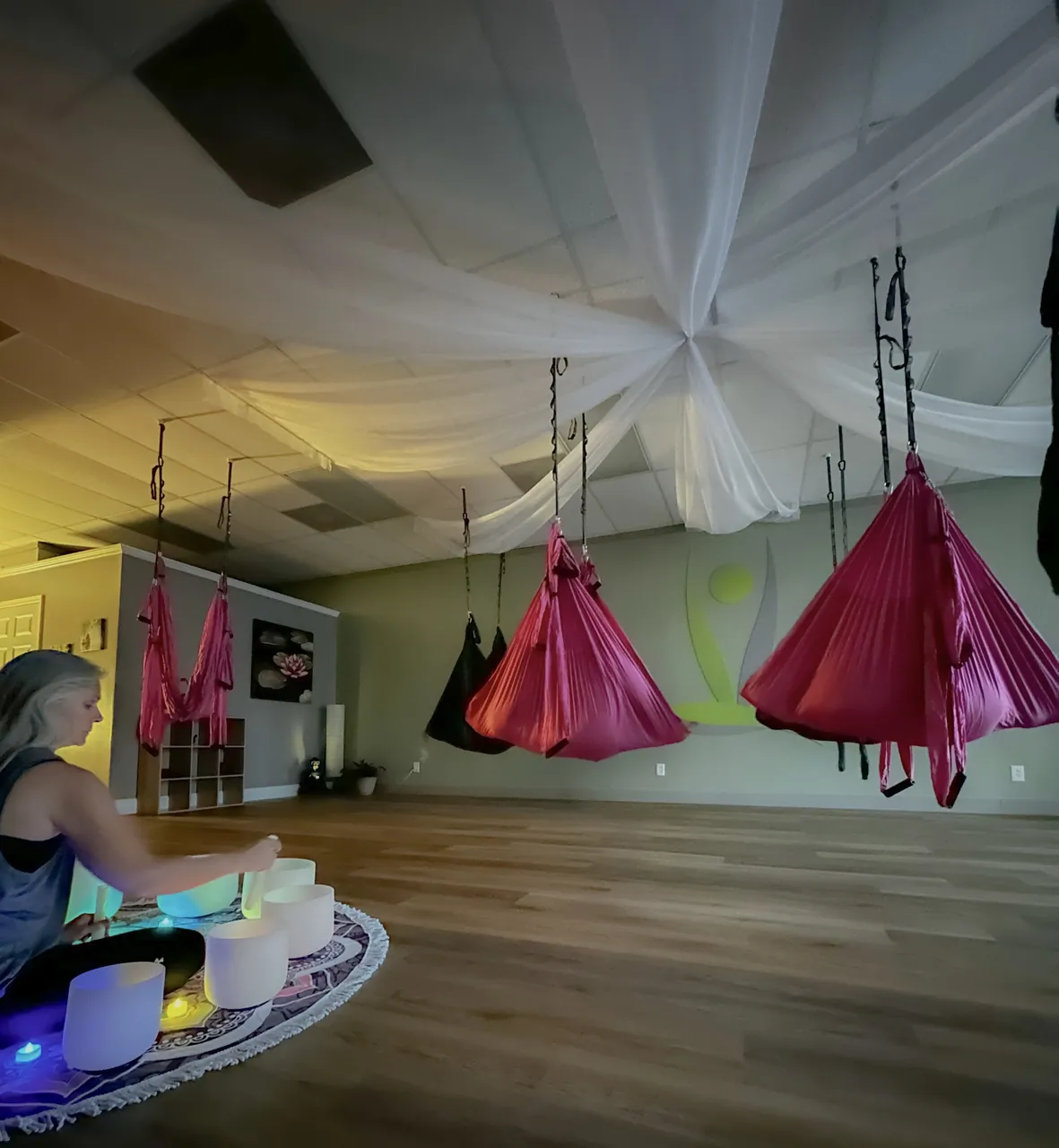 Singing bowls glowing beneath the draped ceiling and hammocks during a sound bath.