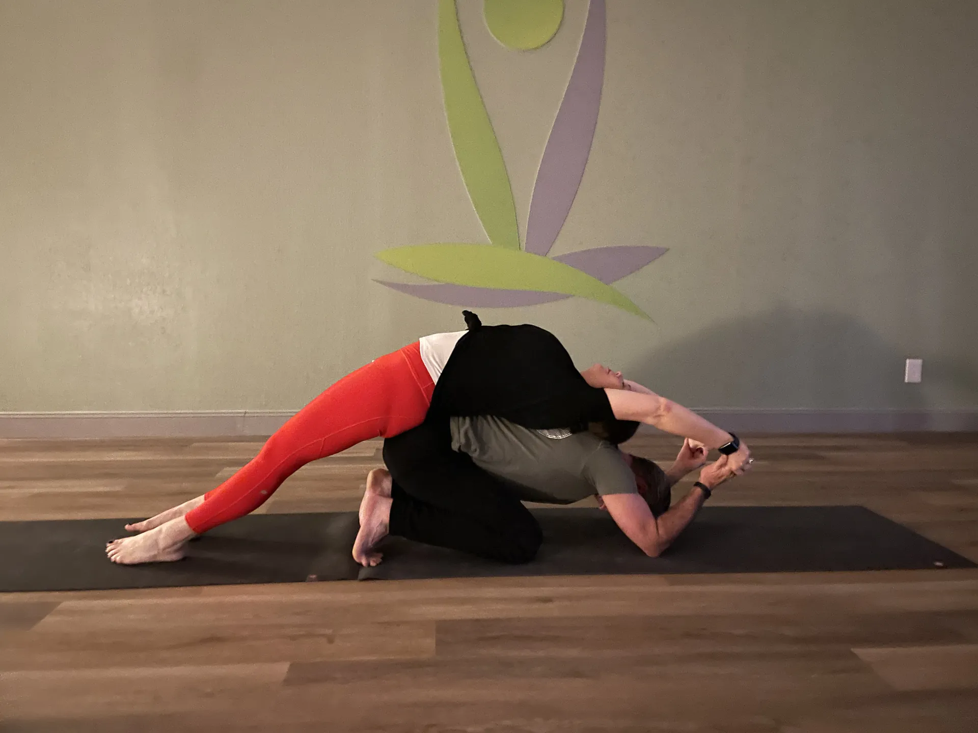 A wide-legged forward fold in front of the studio mural.