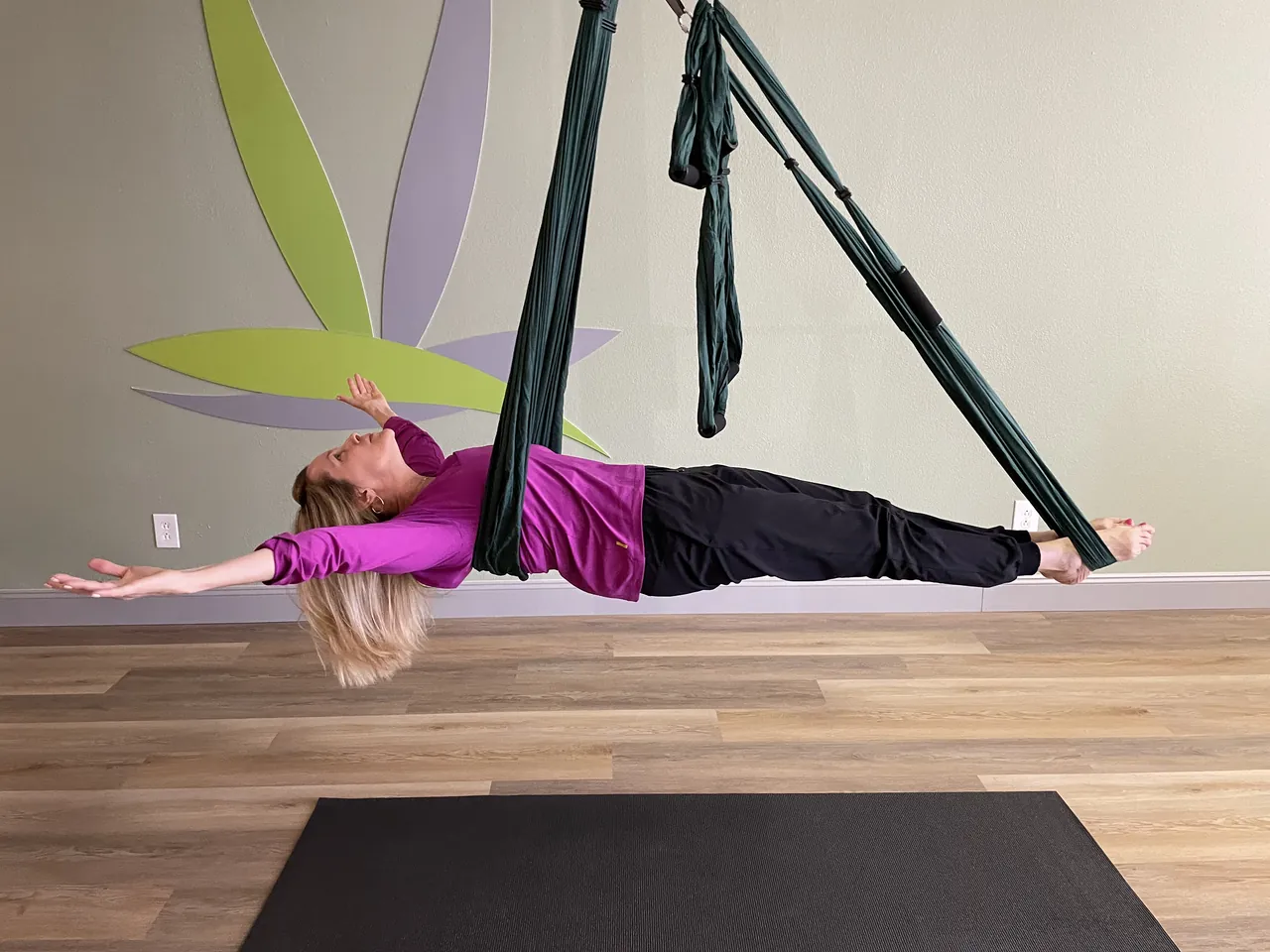 Jill stretched out in the yoga trapeze in front of the mural.