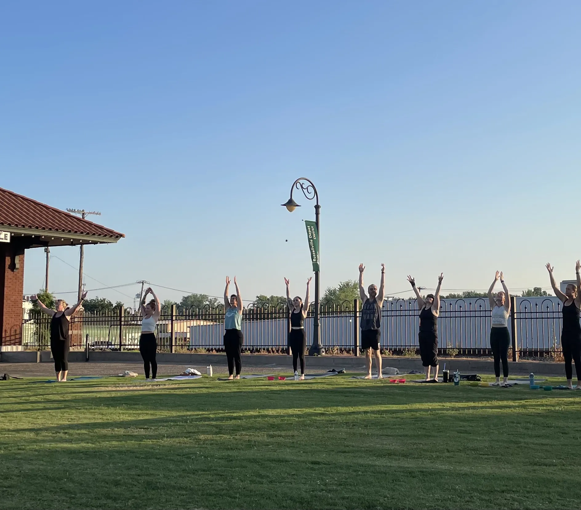 Arms raised in sun salutation on the lawn at the Summer Solstice celebration.
