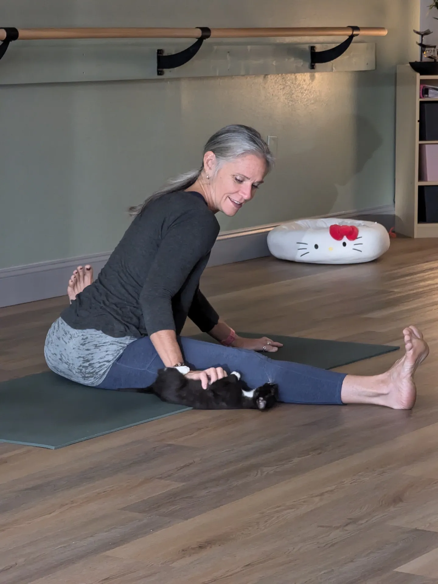 Jill in a seated forward fold with a kitten on the mat.