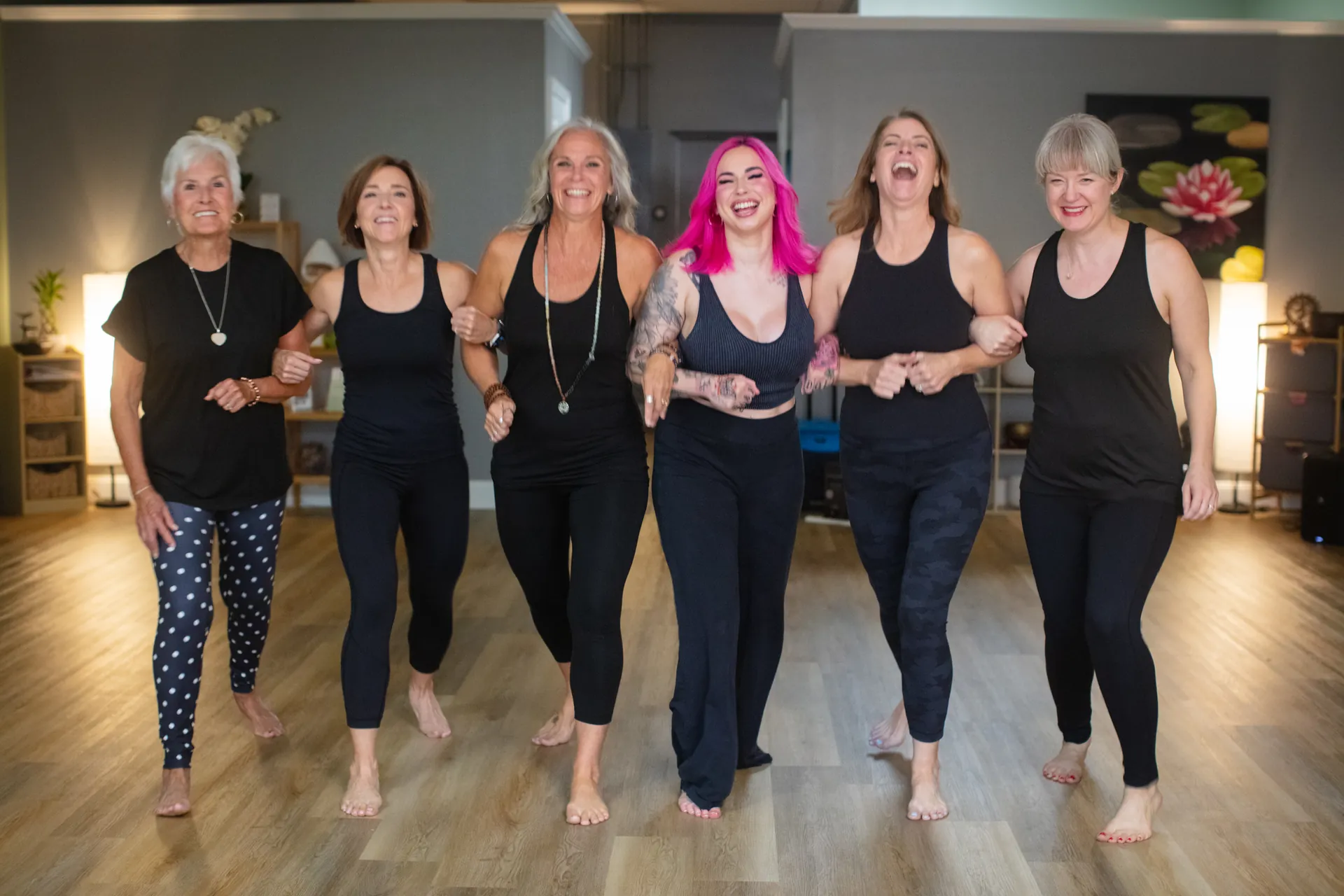 The JB Wellness instructors walking arm in arm across the studio, laughing.